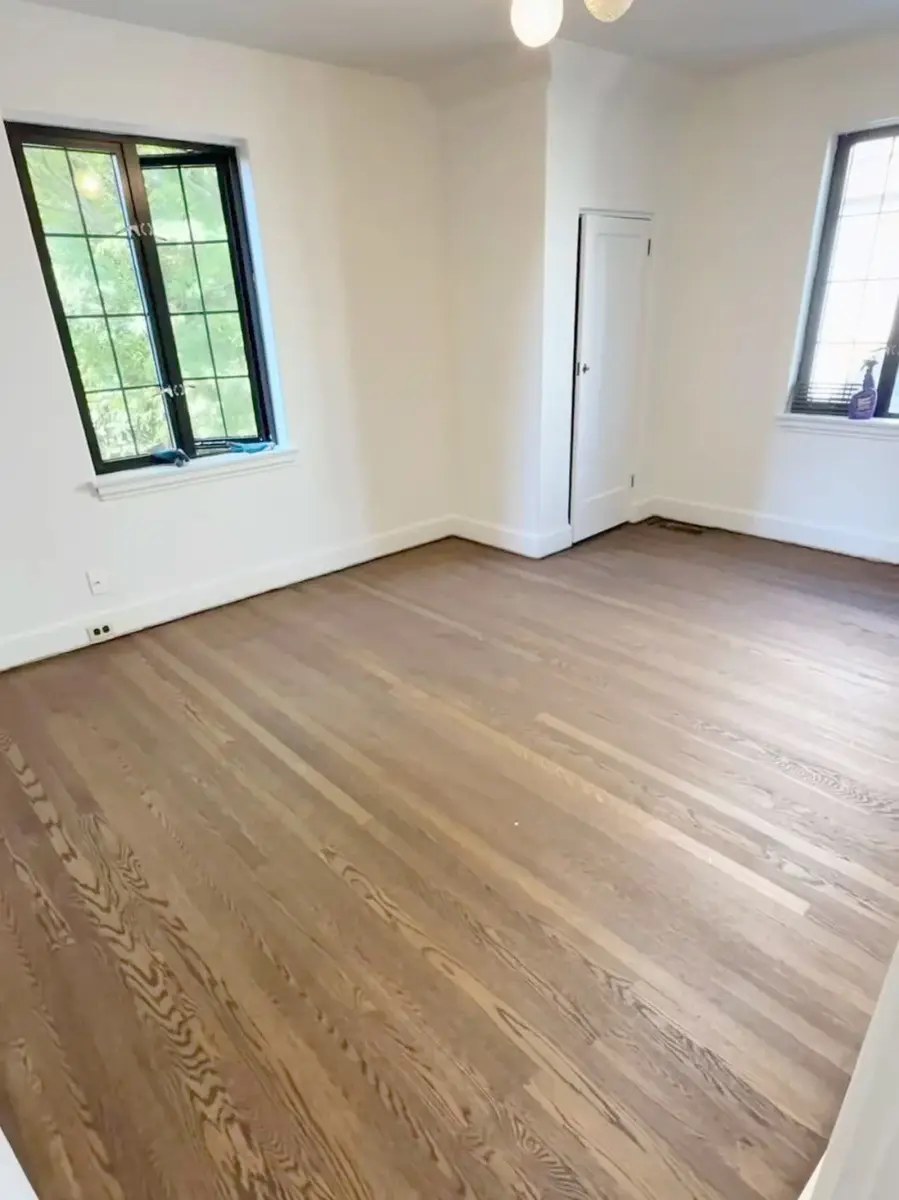Light wood flooring in an empty room with white walls and black-framed windows